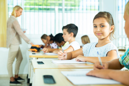Girl sits at a desk next to diligent elementary school studentsの写真素材