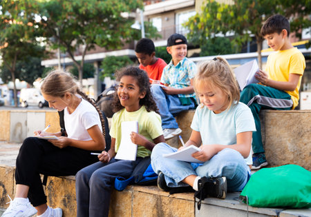 Tweenagers studying outside school, writing in workbooksの写真素材