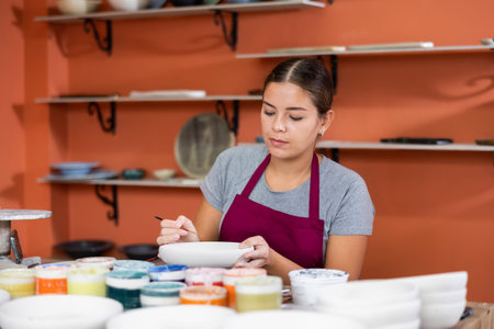 Young woman ceramist painting new crafted plateの写真素材