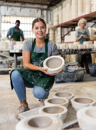 Positive young worker demonstrates half of plaster mold for pottery in pottery factoryの写真素材