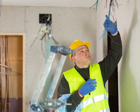 Experienced friendly electrician laying electric wires in building under constructionの写真素材
