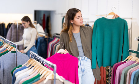 Thoughtful young woman choosing between raspberry and green sweaters in a clothing storeの写真素材