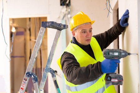 Male contractor holding electric perforator ready for construction works indoors