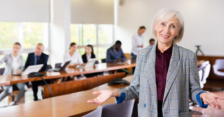 Portrait of an elderly successful businesswoman in meeting room against the backdrop of team of her...