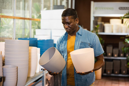 Focused african american greenhouse owner choosing plant pots in storeの写真素材