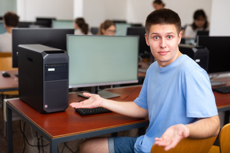 Young male student turned around and looking at camera during lesson in computer class, throwing up handsの写真素材
