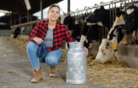 Female farmer with large metallic milk can in hangar with cows