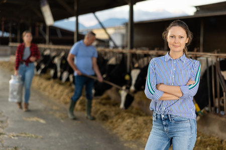Cheerful woman posing in cowshed on farm breeding dairy cowsの写真素材