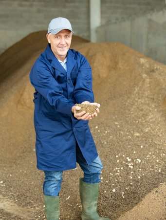 Portrait of mature man farmer holding handful of calf feed in animal feed warehouseの写真素材