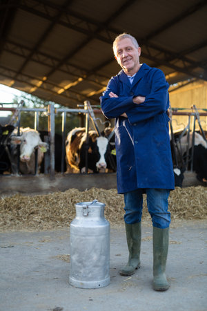 Positive man farmer in cowshed at milk canの写真素材