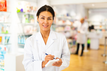 Positive female pharmacist writes in a notebook in the trading floor of pharmacyの写真素材