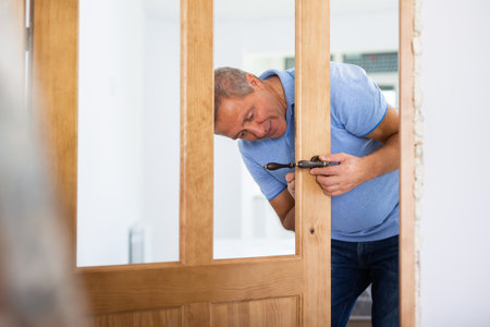 Focused middle-aged repairman checking a doorknob on a door in the houseの写真素材