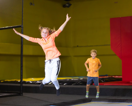 Full length of happy teenage girl in sportswear having fun while jumping high on colorful trampoline at game clubの写真素材