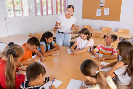 Female teacher conducting lesson with preteen children sitting around deskの写真素材
