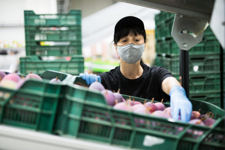 Woman in mask sorting mangoes at warehouse