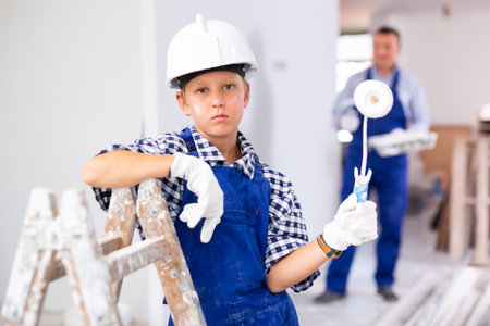 Portrait of pensive boy in coverall and helmet with paint rollerの写真素材