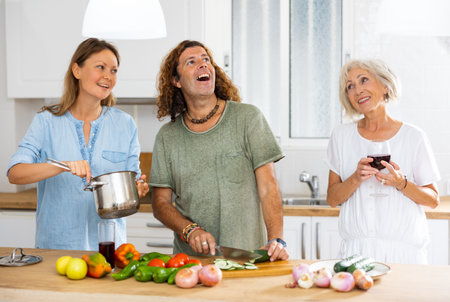 Happy couple and mature female cooking together and drinking wine at the kitchenの写真素材