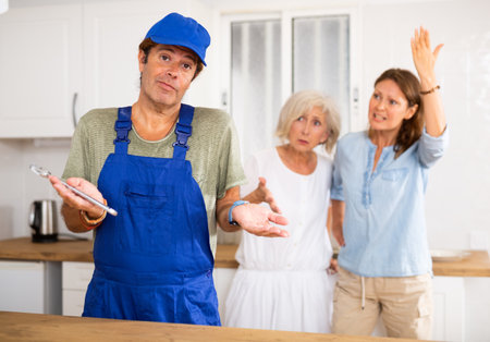 Inept plumber throws up his hands. In background, disgruntled apartment owners scold himの写真素材
