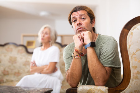 Upset man sitting while quarrel with wife at home interiorの写真素材