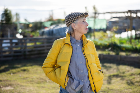 Portrait of elderly woman in yellow jacket and cap in autumn garden