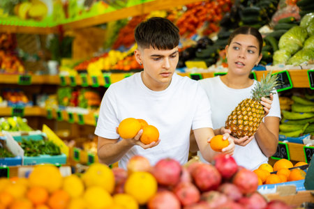 Portrait of happy couple in grocery supermarket, holding oranges and pineapple in their handsの写真素材