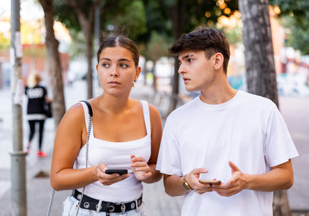 Young man and woman using smartphones outdoors