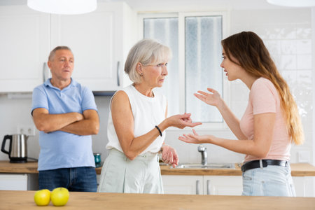 Elderly father tries to calm quarreled wife and daughter in home kitchenの写真素材