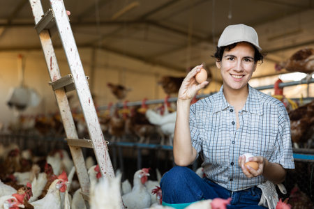 Successful hispanic woman farmer showing chicken eggs in henhouseの写真素材