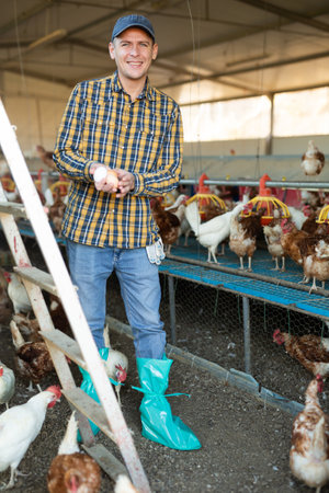 Successful farmer posing in chicken coop with eggs in handsの写真素材