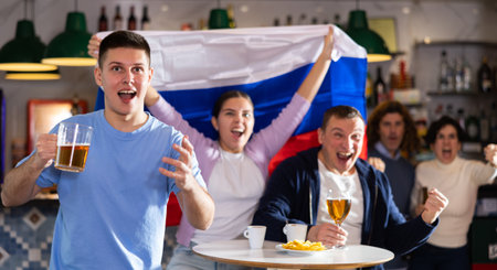 Happy friends of different ages drinking beer and celebrating the victory of the Russian team in night barの写真素材
