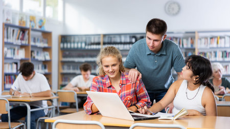 Smiling boy helping positive pupils research, working with laptop in library