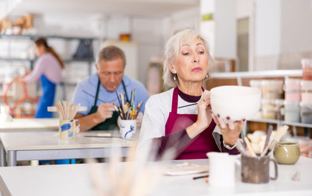 Mature woman painting clay ceramic at art studio