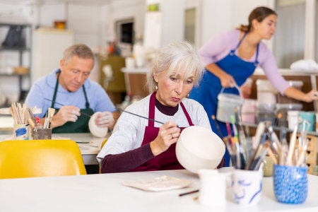 Woman potter with paintbrush, painting on plate in workshop, working in studio
