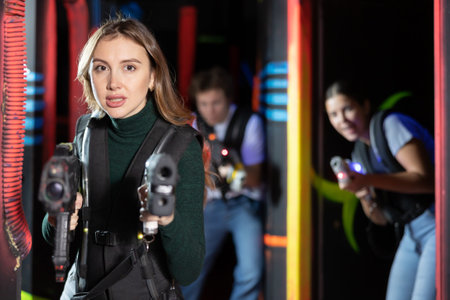 Smiling girl with laser pistol during playing laser tag with her friends in room