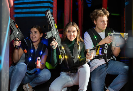Modern young people with laser pistols playing laser tag on dark labyrinthの写真素材