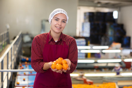 Happy female fruit sorting factory worker holding tangerines