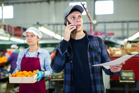 Young supervisor with papers talking on phone in citrus sorting factory