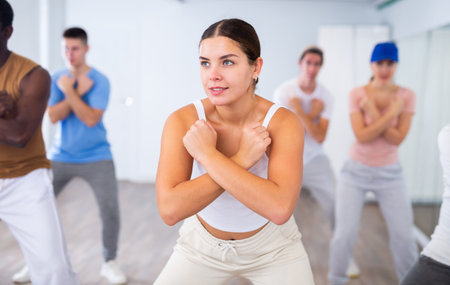 Group of young adult diverse active dancers in sportswear with crossed hands during dance exercise...