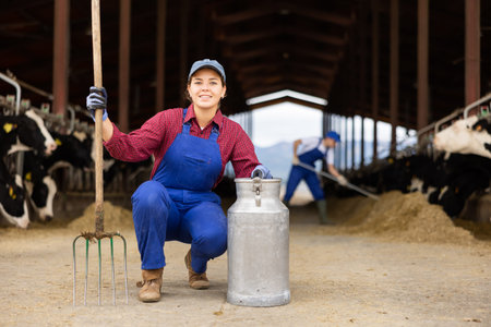 Farmer woman holds rake and can at cow farm