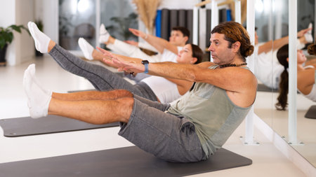 Middle-aged man practicing pilates on gray mat in gym room