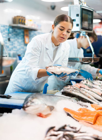 Positive saleswoman demonstrating seabass in fish store