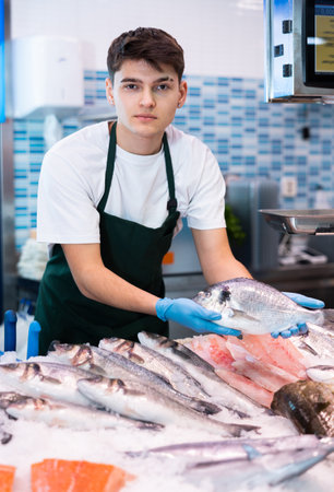Smiling salesman demonstrating seabass in fish storeの写真素材