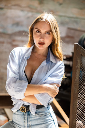 Young woman in jeans and tied shirt posing in destroyed plant