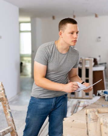 Fifteen-year-old worker fills out paperwork on a construction site indoorsの写真素材