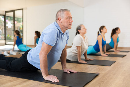 Class of male and women of different ages in active wear doing cobra exercise exercise during...