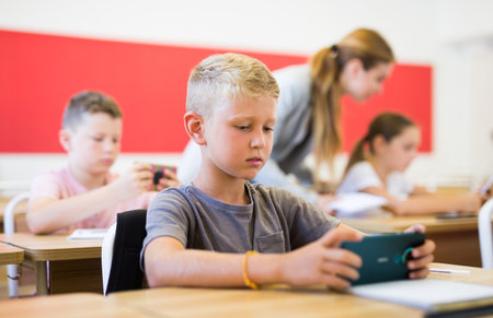 Absorbed preteen boy using smartphone at lesson in schoolの写真素材
