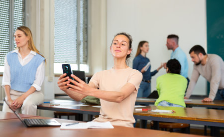 Positive young female student takes selfie in front of a group of students in university auditoriumの写真素材