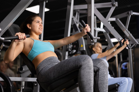 Young woman trains her arm muscles using a simulator in gymの写真素材