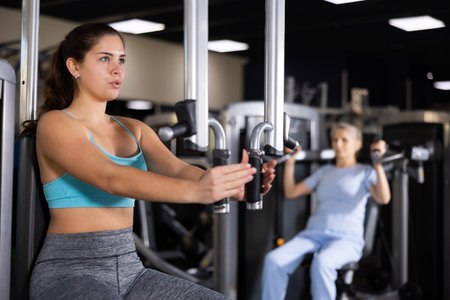 Athletic woman is engaged in simulator - develops biceps and triceps