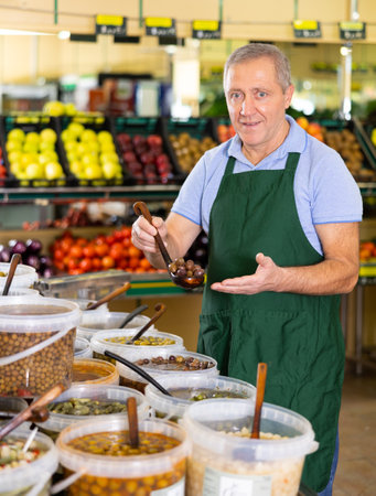 Elderly salesman showing olives in grocery storeの写真素材